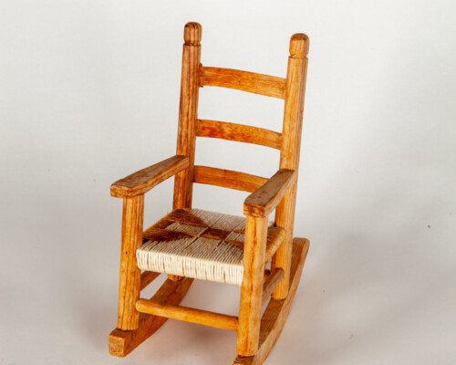 Dollhouse rocking chair. Medium tone wood and woven seat.