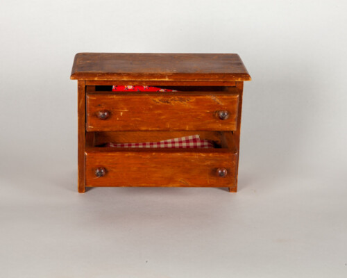 Dollhouse dresser. Darker wood with red patterned fabric peaking from drawers.