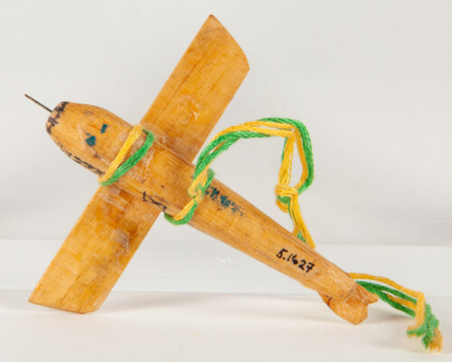 Underside of toy plane. Yellow and green twine attaches the wings to the plane.