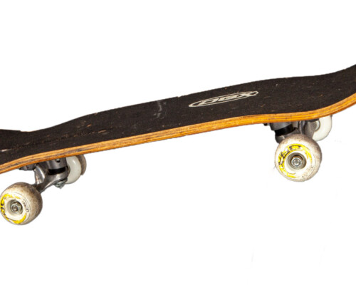 Side of DBX skateboard, shows wear on the trucks and wheels.