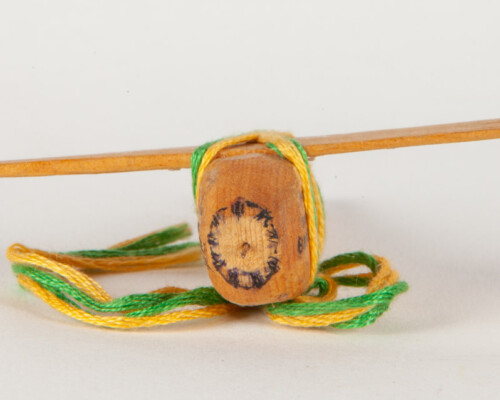 Front of Handmade toy plane. Carved image of an engine face and yellow and green twine sits below.