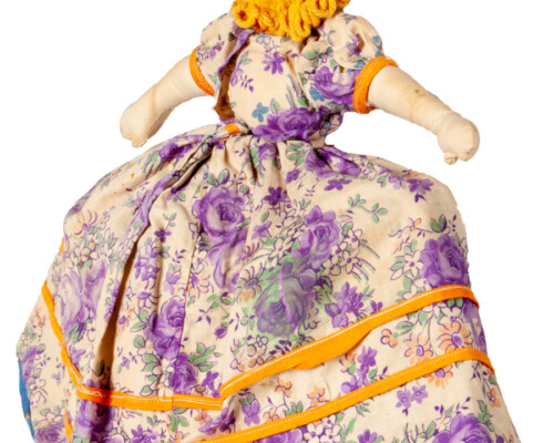 Rear side of blonde doll with blue and tan floral dress.