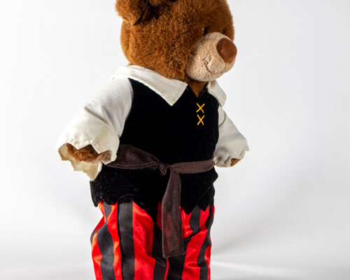 Side view of teddy bear in black, red, and white pirate outfit.