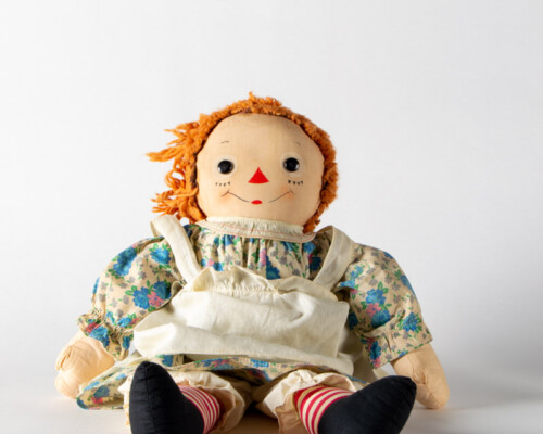 Side view of Raggedy Anne doll sitting with short hair and blue and tan floral dress.